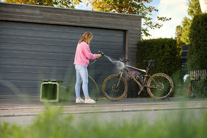 Frau in pinkem Pullover und Jeans mit Kärcher WBS 3 Reinigungspistole auf schmutzigem Mountainbike